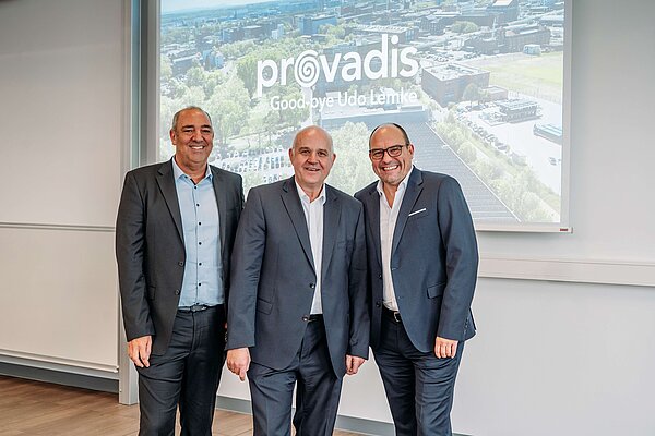 Drei Personen in Business-Outfits stehen vor der Leinwand mit dem Schriftzug „Provadis – Goodbye Udo Lemke“ zusammen, symbolisch für den Führungswechsel bei Provadis und die Zusammenarbeit mit Infraserv Höchst.