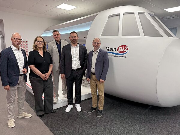 Besuch von Vertretern im MainBiz Informationszentrum. Gruppenfoto vor einem Flugzeugmodell.