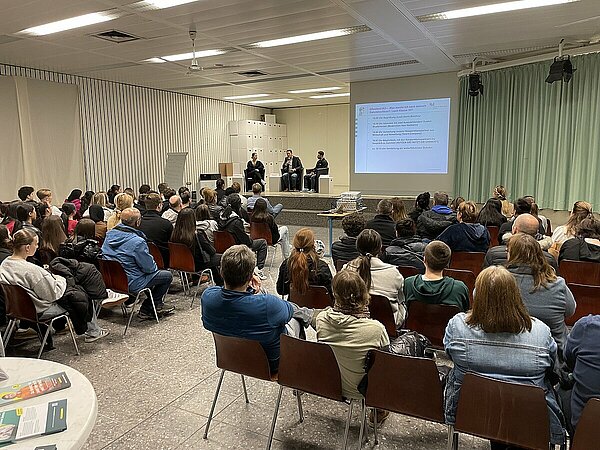 Publikum schaut Podiumsdiskussion zu. Menschen bei einer Präsentation.