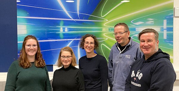 Gruppe von fünf Personen vor einem bunten Hintergrund.